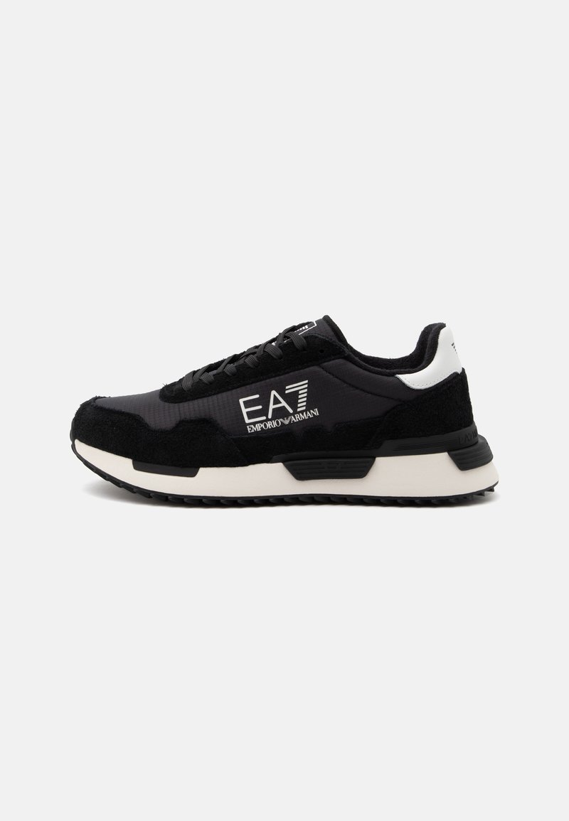 Μαύρο και άσπρο sneaker Emporio Armani EA7 με σχεδιασμό κορδονιών και παχιά σόλα, εμφανίζεται από το πλάι σε απλό φωτεινό φόντο.