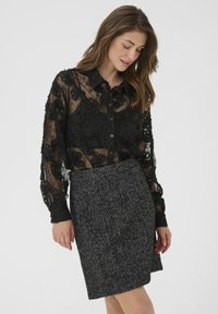 Blusa nera in pizzo con motivo floreale e chiusura a bottoni, abbinata a una gonna a tubino in tessuto a scacchi bianco e nero.