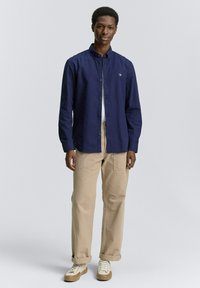 Camisa de botones azul marino de algodón con cuello clásico, combinada con pantalones cargo color beige y zapatillas blancas con detalles en beige.