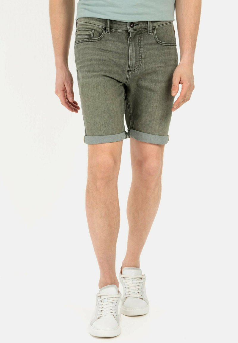Olijfgroene denimshorts met een omgeslagen zoom, voorzien van een klassiek 5-pocket ontwerp en een ritssluiting, gecombineerd met witte sneakers.
