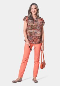Camicia a maniche corte con fantasia multicolore, abbinata a pantaloni corallo. Le scarpe flat grigie e una piccola borsa arancione completano il look.