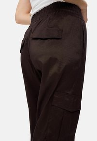 Hnedé cargo nohavice s textúrovaným povrchom, vybavené elastickým pásom a náprsnými vreckami po oboch stranách.