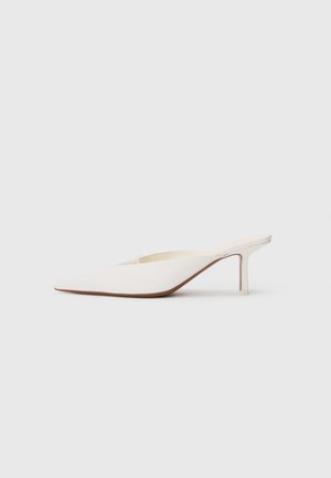 Spetsig tå vit mule med en låg stilettklack. Tillverkad av mjukt material med en minimalistisk design och subtila bruna souldetaljer.