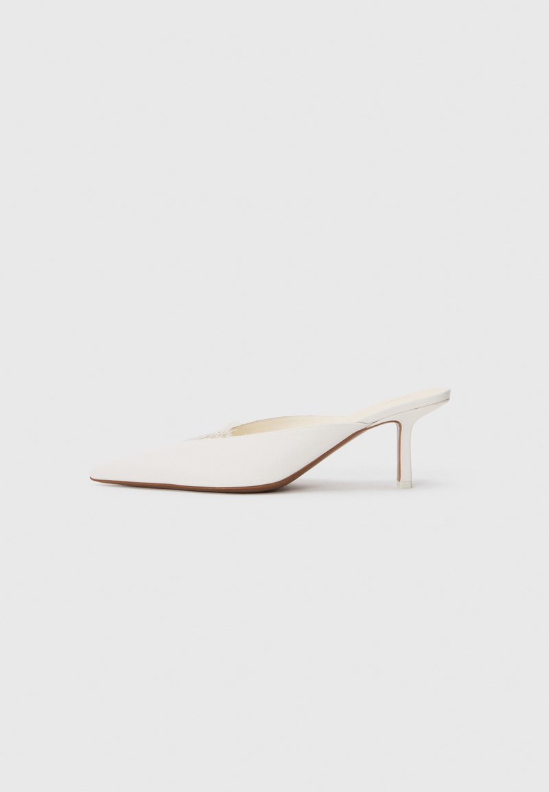 Spetsig tå vit mule med en låg stilettklack. Tillverkad av mjukt material med en minimalistisk design och subtila bruna souldetaljer.