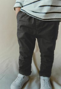 Grå, strukturerede bukser med elastisk talje, forlommer og syet detalje, parret med hvide sneakers. Toppen har marineblå striber på creme.