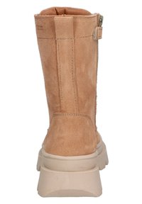 Botín de ante color beige claro con suela blanca gruesa. Presenta un zip lateral y un pequeño lazo para facilitar su uso. Acabado ligeramente texturizado.