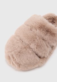 Puha, plüss bézs mamusz, mely szőrhatású textúrával, kerek formával és három vízszintes párnázott résszel rendelkezik. Nincsenek látható zsanérok vagy minták.