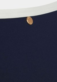 Námornícka plavková látka s bielym elastickým pásom. Obsahuje okrúhly bronzový cvok s vygravírovaným logom. Hladká, pružná textura.
