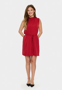 Robe rouge avec un col montant et un design sans manches. Présente une taille à cordon, une longueur jusqu'aux genoux et une texture de tissu lisse.