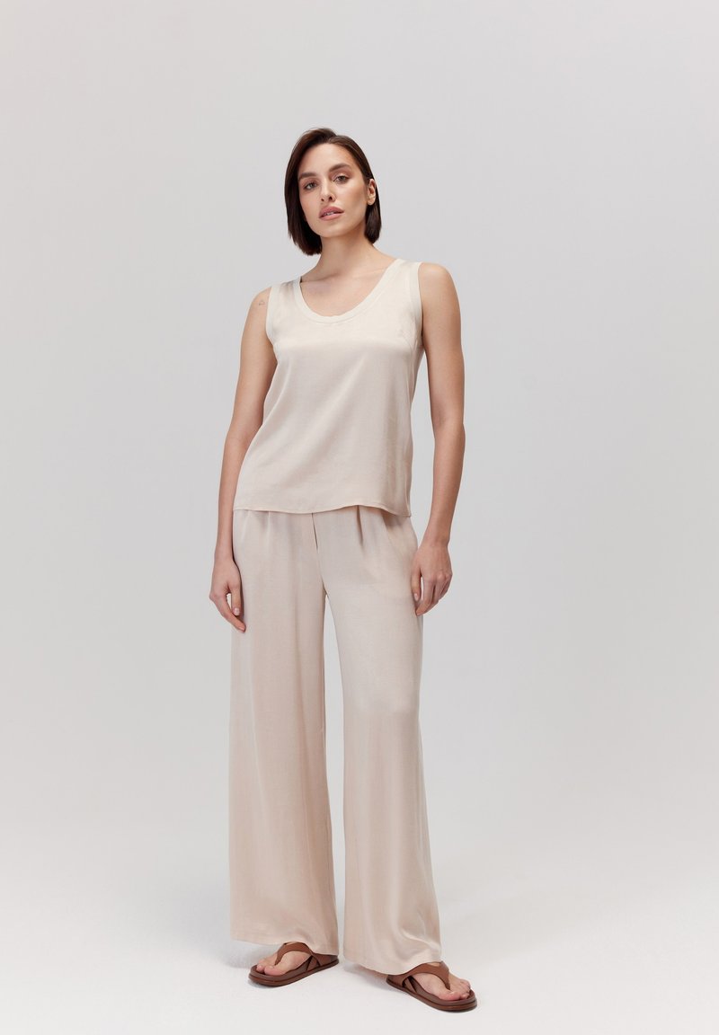 Beżowy top na ramiączkach i szerokie spodnie z lekkiego materiału, charakteryzujące się luźnym krojem i gładką teksturą. Brązowe klapki dopełniają całość.