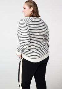 Gestreepte trui in crème en marine met een losse pasvorm, geribbelde manchetten en een bandzoom. Zwarte broek met een crèmekleurige zijkstreep.