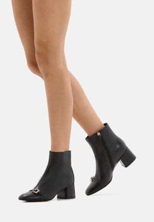 Stivaletti neri in pelle con tacco a blocco, zip laterale e accessori decorativi sul davanti. Texture liscia e design aderente.