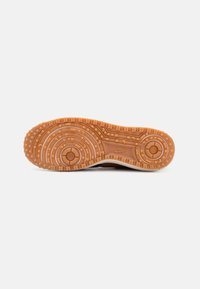 Nike sneaker talpa világosbarna színben, körkörös és hullámos mintákkal, texturált részletekkel és fehér középtalppal.