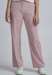 Rosa brede bukser lavet af glat stof, med en frontfold og diskrete lommer, parret med hvide sneakers.