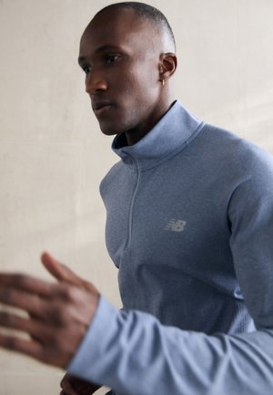 Pull-over bleu clair à zip quart, fabriqué en matériau texturé, avec des manches longues et un logo discret sur la poitrine. Fini lisse.