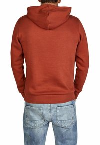 Rust-colored hoodie with a kangaroo pocket and adjustable hood, paired with light blue denim jeans featuring stitched pockets.