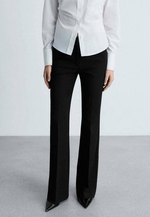 Pantaloni neri su misura con design a campana, realizzati in un tessuto morbido. Abbinati a una camicia bianca con bottoni e tacchi appuntiti neri.