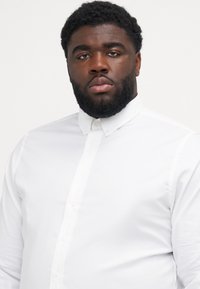 Camicia bianca con bottoni realizzata in tessuto morbido, con colletto classico e maniche lunghe, caratterizzata da un design slim-fit e dettagli di cucitura discreti.
