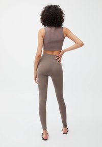 Bruine geribde cropped top gecombineerd met hoog-taille bruine geribde leggings. Beide hebben een gladde textuur en een aansluitend ontwerp. Sandalen accentueren de look.