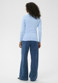 Haut en maille bleu clair à manches longues avec une coupe ajustée, associé à un jean en denim bleu à jambes larges. Texture lisse, style décontracté, sans motifs notables.