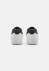 Valged nahk-sneakerid mustade kandetailide, õmblustega ja tasase valge tallaga. Tagant vaadatuna toob esile sujuva tekstuuri ja värvi kontrasti.
