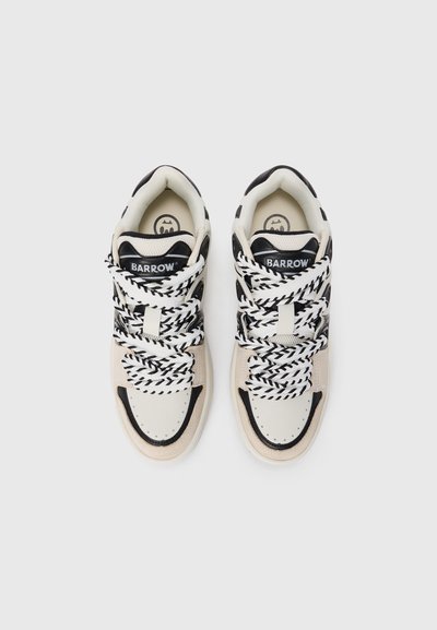 Sneakers in cream and black leather with textured laces, featuring a padded collar and logo on the tongue. Rounded toe and low profile.