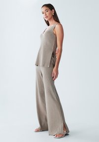 Beżowy, prążkowany top na ramiączkach z bocznymi rozporkami, w połączeniu z szerokimi spodniami typu wide-leg, charakteryzującymi się luźnym krojem i gładką fakturą. Obuwie to sandały na paski.
