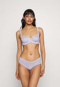 Intimo di colore lavanda chiaro con bordi scallop. Il reggiseno presenta coppe strutturate e le mutandine hanno una texture morbida e trasparente.