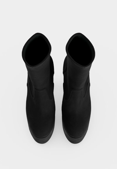 Paire de bottes noires mi-mollet vues d'en haut sur un fond blanc uni.
