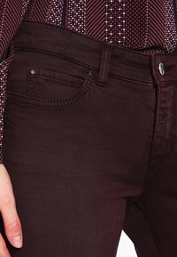 Džínové kalhoty barvy burgundské se sametovou texturou, s pěti kapsami a zapínáním na kovový knoflík. Disponují minimálním šitím a jemnými detaily.