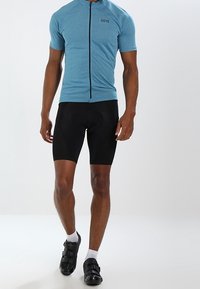 Krátký světle modrý cyklistický dres s předním zipem a logem, doplněný černými polstrovanými šortkami a černými cyklistickými botami.