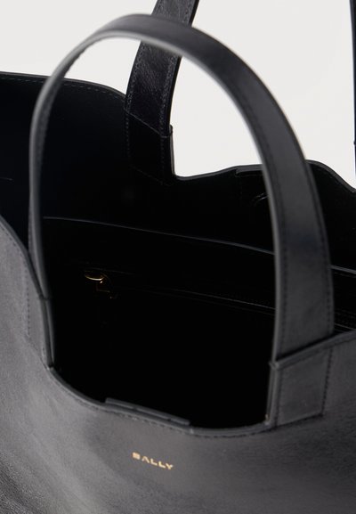 Μαύρη δερμάτινη τσάντα ώμου με ραμμένες λαβές και μικρό χρυσό λογότυπο στο μπροστινό μέρος, ανοιχτή για να δείξει το ευρύχωρο εσωτερικό της.