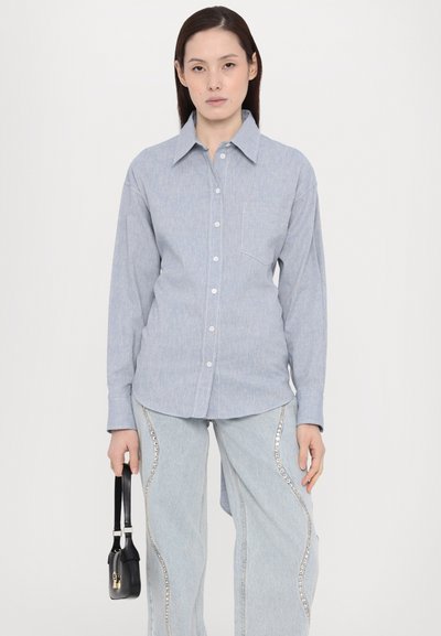 Lyseblå langermet skjorte med knapp- ned krage, brystlomme og subtilt teksturert mønster, kombinert med blå jeans med metalliske detaljer.