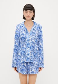 Blue and white patterned pajama set featuring a long-sleeve button-up top and matching shorts, made from lightweight fabric with a smooth texture.