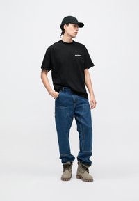 Camiseta negra de algodón con logo, pantalones vaqueros azules de corte relajado y botas grises con superficie texturizada y diseño con cordones.