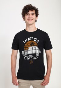 Černé bavlněné tričko s grafikou vintage auta, s textem "NEJSEM STARÝ, JSEM KLASIKA" a pozadím oranžového západu slunce.