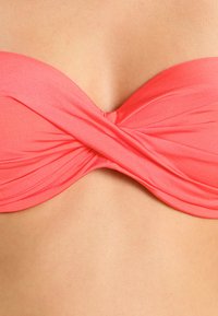 Top de bikini bandeau cor-de-rosa coral com design de frente torcida, textura suave e sem hardware visível. Adequado para uso em banho.