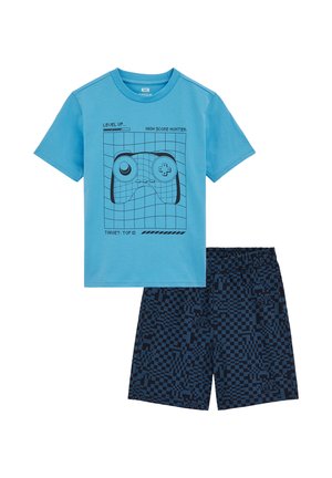 Svetlo modra majica s črnim grafičnim prikazom igralnega krmilnika, združena z mornarsko modrimi hlačami s pikseliranim vzorcem in elastičnim pasom.