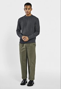 Donkergrijze kabelgebreide trui met lange mouwen, gecombineerd met olijfgroene wijde broek en zwarte veterschoenen. Eenvoudig, textuurontwerp.