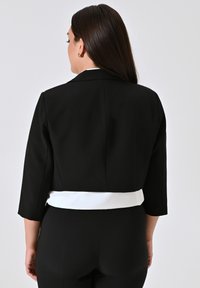 Zwarte cropped jacket met driekwart mouwen, met een witte tailleband detail. Gladde stof met gestructureerd ontwerp.