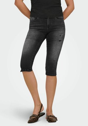 Woman wearing black mid-length skinny jeans with slight distressing and leopard print flat slingback shoes against a plain background.