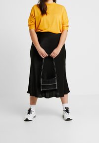 Top amarillo de manga corta, falda midi de satén negra y zapatillas blancas. Bolsa negra con acentos de cuentas. Texturas suaves y diseño sencillo.