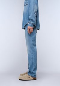 Jeans de mezclilla azul claro con corte recto, combinados con una camisa de manga larga de color azul claro. La persona lleva puestos zapatos de ante beige.
