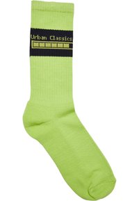 Zöld pamutzokni bordázott textúrával, fekete sávval a tetején, sárga felirattal: "Urban Classics".