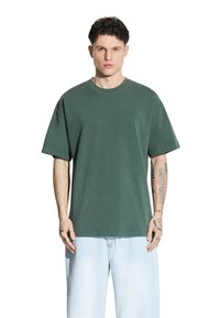 Oliwkowa bawełniana koszulka z luźnym krojem, okrągłym dekoltem i krótkimi rękawami. Posiada subtelny detal z logo oraz miękką, teksturowaną tkaninę.