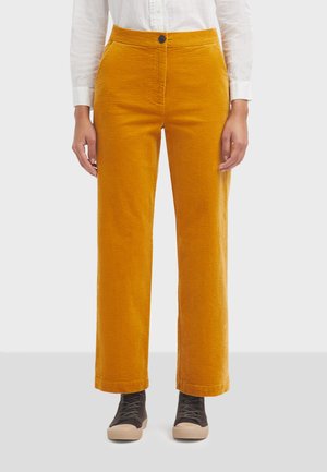 Pantaloni in corduroy giallo senape con design a gamba dritta, chiusura frontale con bottone e tasche laterali, abbinati a sneaker scure.
