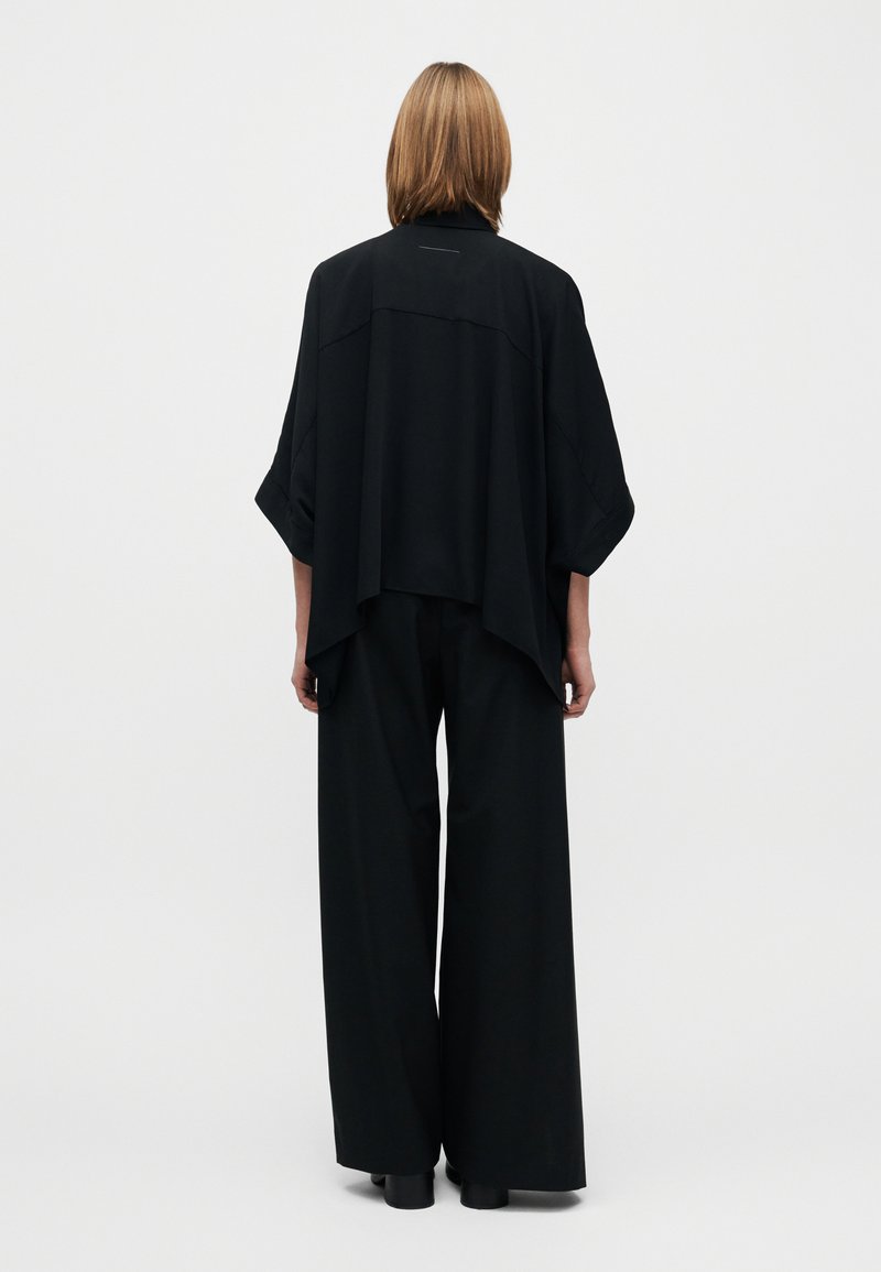 Vêtement noir oversize avec manches larges, pantalon noir à jambe large, design simple, texture lisse et détails subtils de coutures.