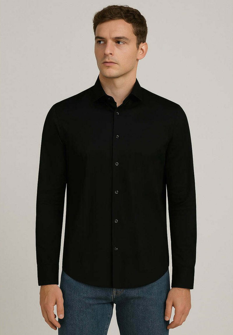 Camicia nera a maniche lunghe in tessuto liscio, con colletto a punta, bottoni frontali e fondo curvo. Indossata con jeans blu.