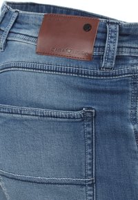 Jasnobłękitne dżinsy z odzieżą o lekko spranionym wyglądzie, z brązową skórzaną łatką marki, detalami przeszycia i klasycznym pięciopocketowym fasonem.