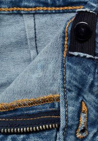 Tessuto denim di colore azzurro chiaro. Presenta cuciture arancioni, una chiusura con bottone nero e un dettaglio con zip aperta su una tasca.